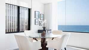 A modern dining area with a glass table, white chairs, and a view of the ocean.