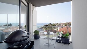 A balcony with a grill, two chairs, and potted plants.