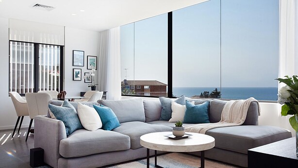 A modern living room with a large grey sectional sofa, a round coffee table, and a view of the ocean.