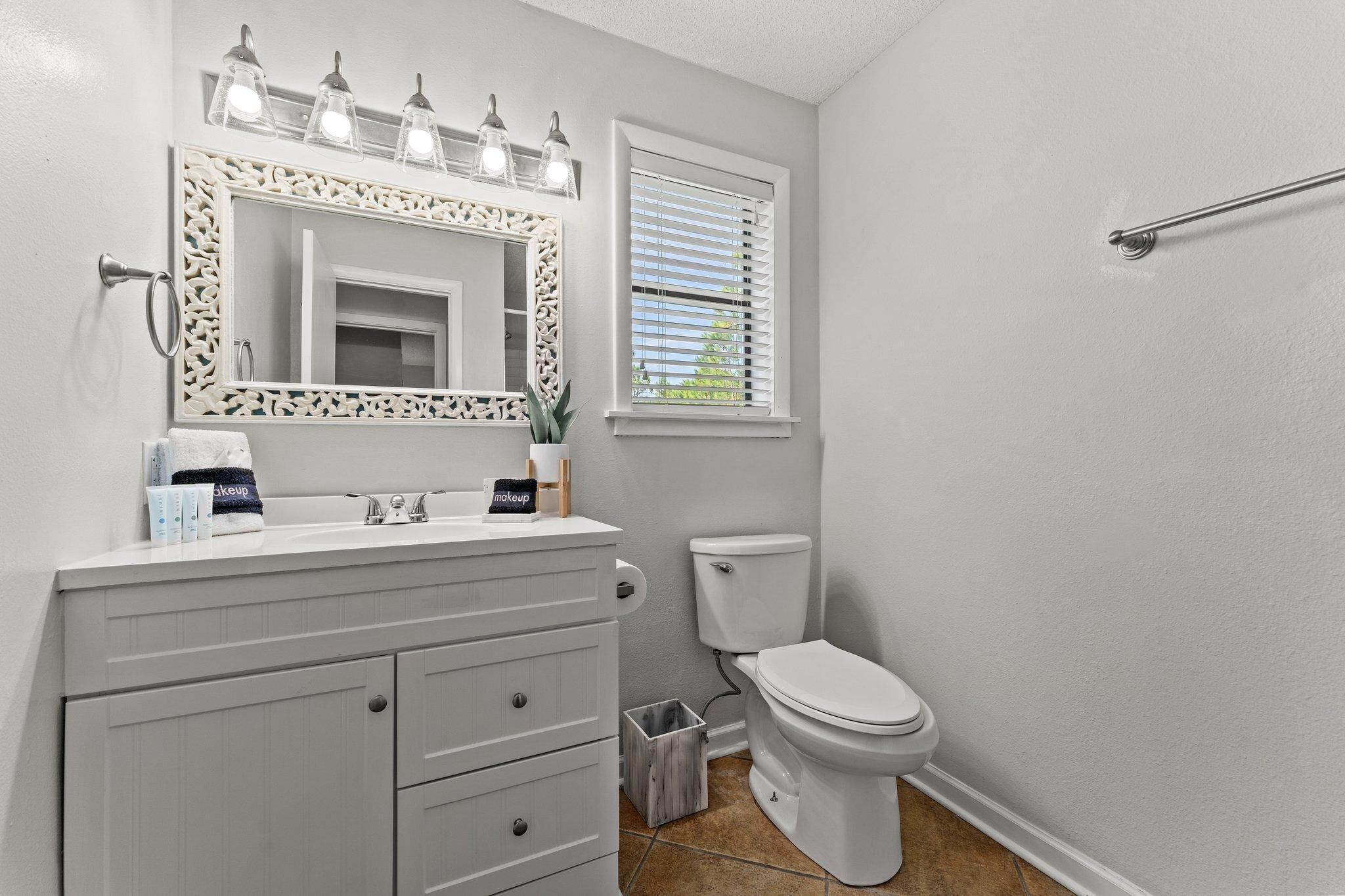 A bathroom with a white vanity, a toilet, and a window with blinds.