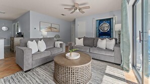 Ein modernes Wohnzimmer mit zwei grauen Sofas, einem runden Holztisch und einem Deckenventilator.