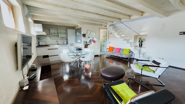 A modern living room with a dining area, a kitchen, and a staircase leading to an upper level.