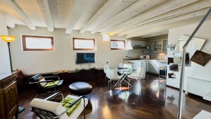A modern living room with a sofa, chairs, and a dining table. There is a kitchen area with a microwave and cabinets. - Arena Deluxe - Duplex apartment with Arena view (Verona)