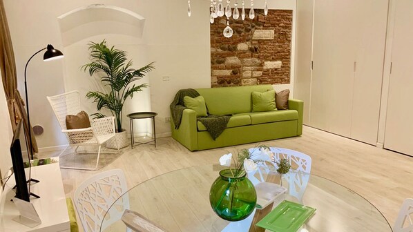 A modern living room with a green sofa, white chairs, a glass coffee table, and a decorative plant. - Casa Verdi (Verona)