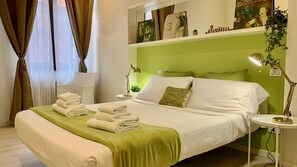 A neatly made bed with folded towels, a bedside lamp, and a green wall with artwork. - Casa Verdi (Verona)