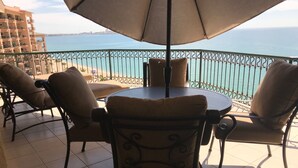 Une terrasse avec une table et des chaises, un grand parasol et une vue sur la mer.
