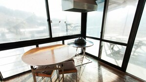Une pièce d’angle avec une grande fenêtre, une table ronde et une petite table ronde avec une lampe.
