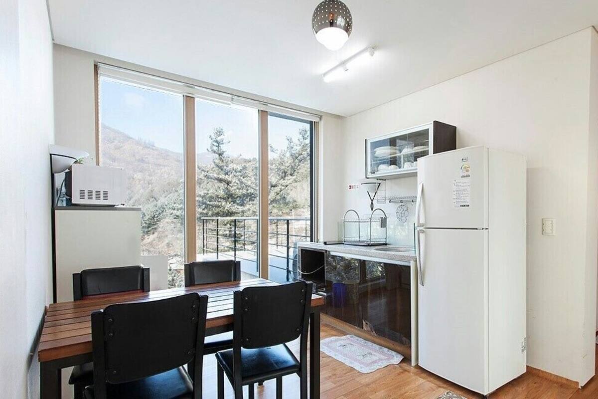 Une cuisine compacte avec un coin repas, de grandes fenêtres et une vue sur les arbres.