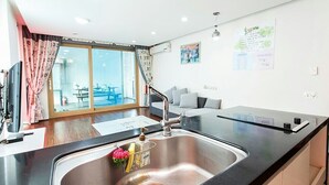 Une cuisine moderne dotée d’un évier en acier inoxydable, d’un coin repas avec une table et des chaises, et offrant une vue dégagée grâce à de grandes fenêtres.
