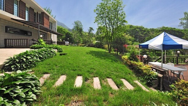 Un jardin bien entretenu, avec une pelouse, des allées en bois et un espace extérieur aménagé avec des sièges, le tout abrité sous une tente.