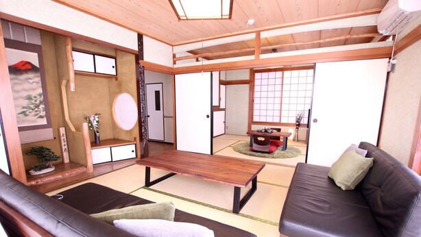 A traditional Japanese-style living room with tatami flooring, a low wooden table, and a sofa. - Mahoroba (Motobu)