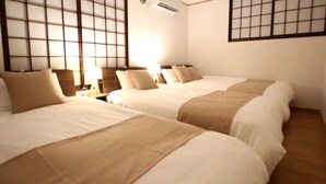 A hotel room with two beds, a traditional sliding door, an air conditioning unit, and a bedside table with a lamp. - Mahoroba (Motobu)