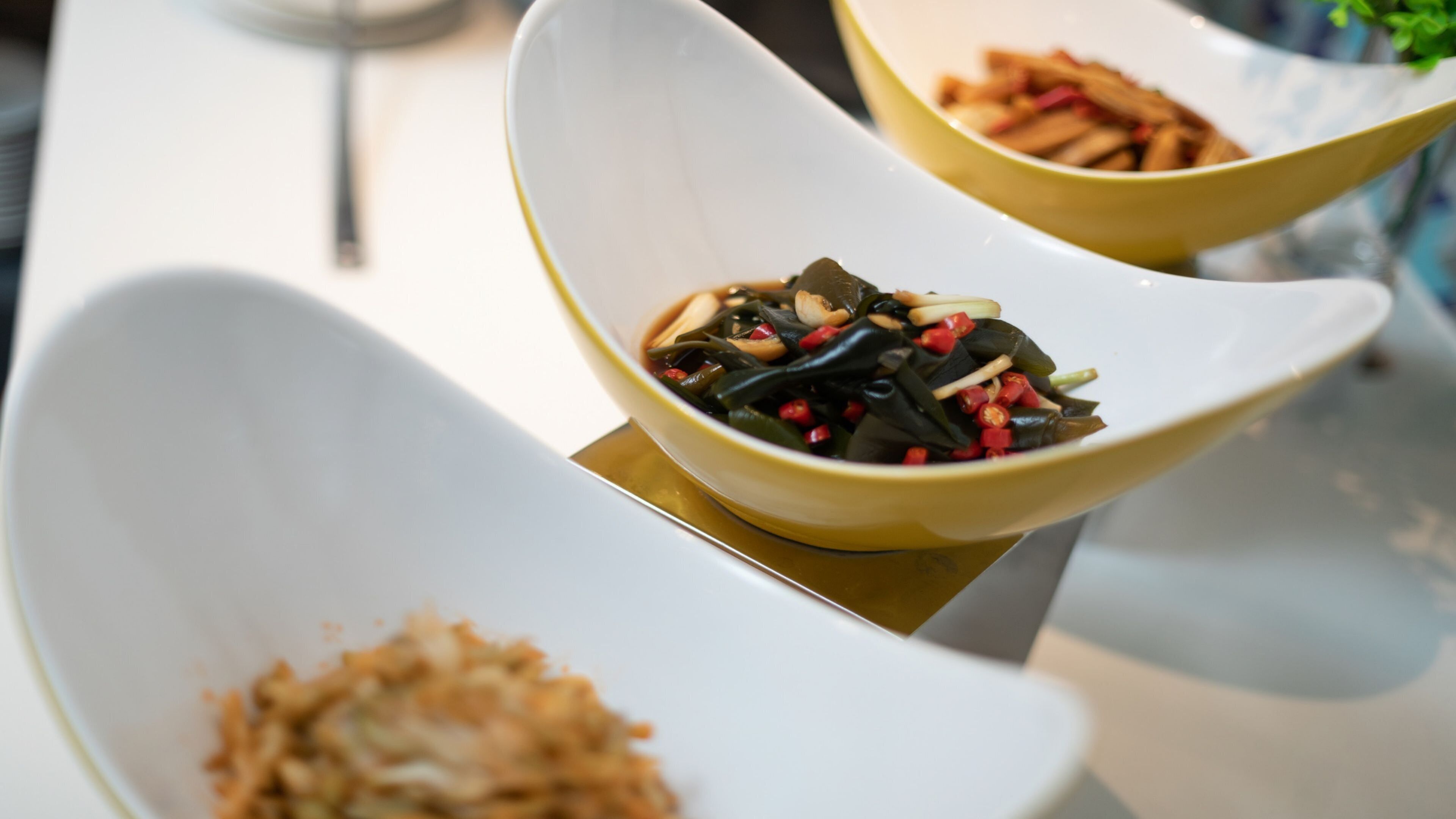 Une table à manger avec trois plats blancs, en forme de bol, contenant différents types d’aliments.