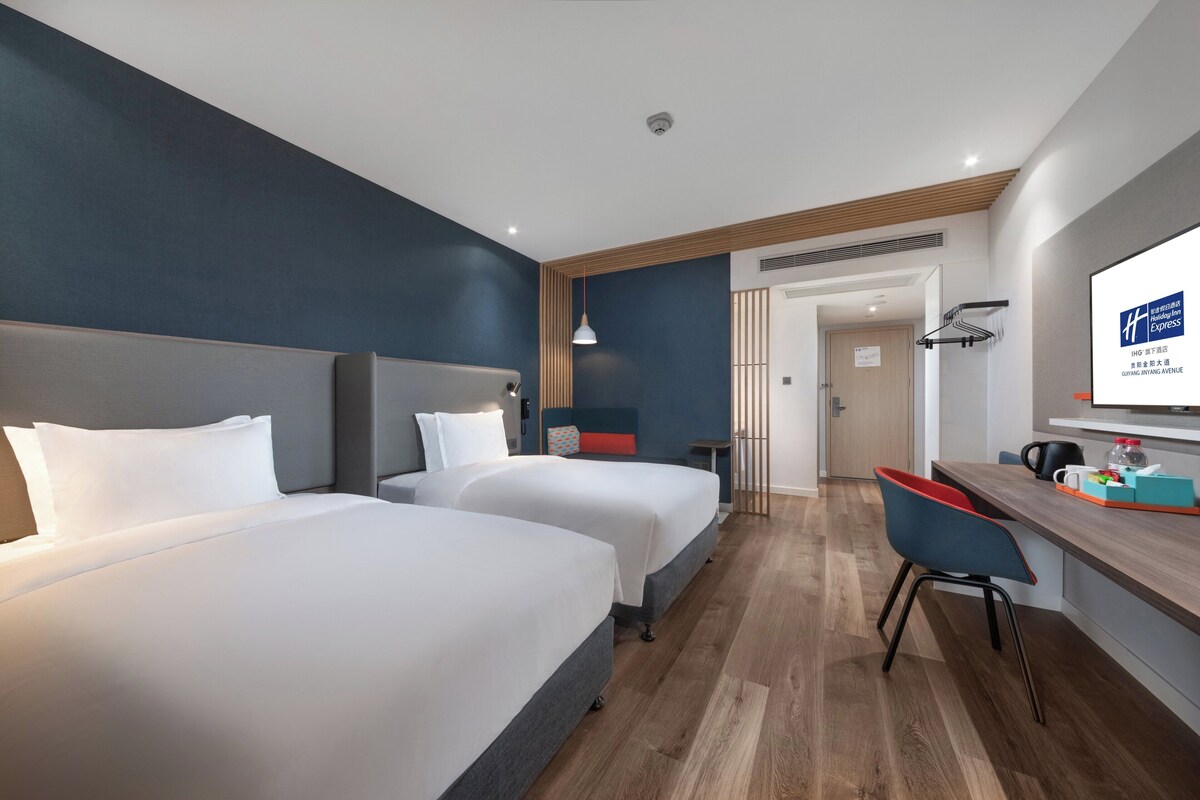 A hotel room with two beds, a desk, and a chair.