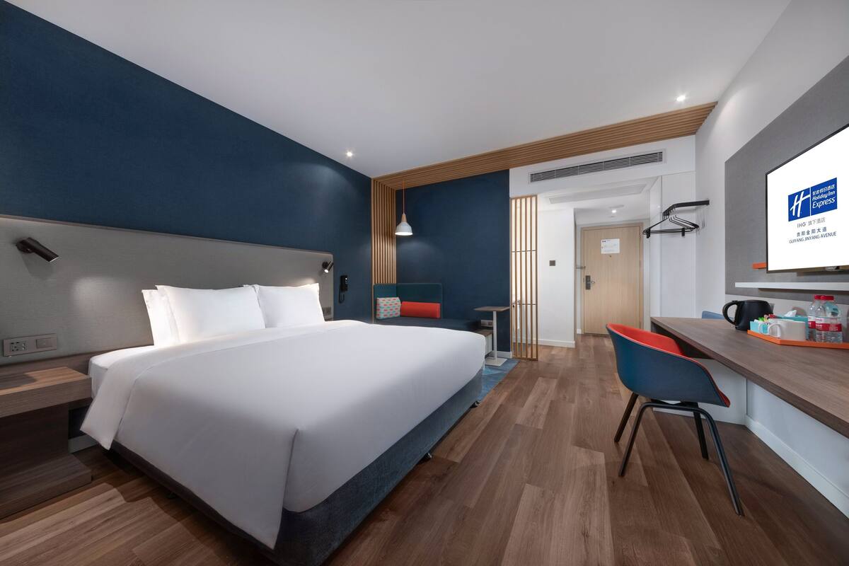 Une chambre d’hôtel moderne avec un grand lit, un bureau et une chaise. Un téléviseur est fixé au mur et une porte donne accès à la salle de bain.