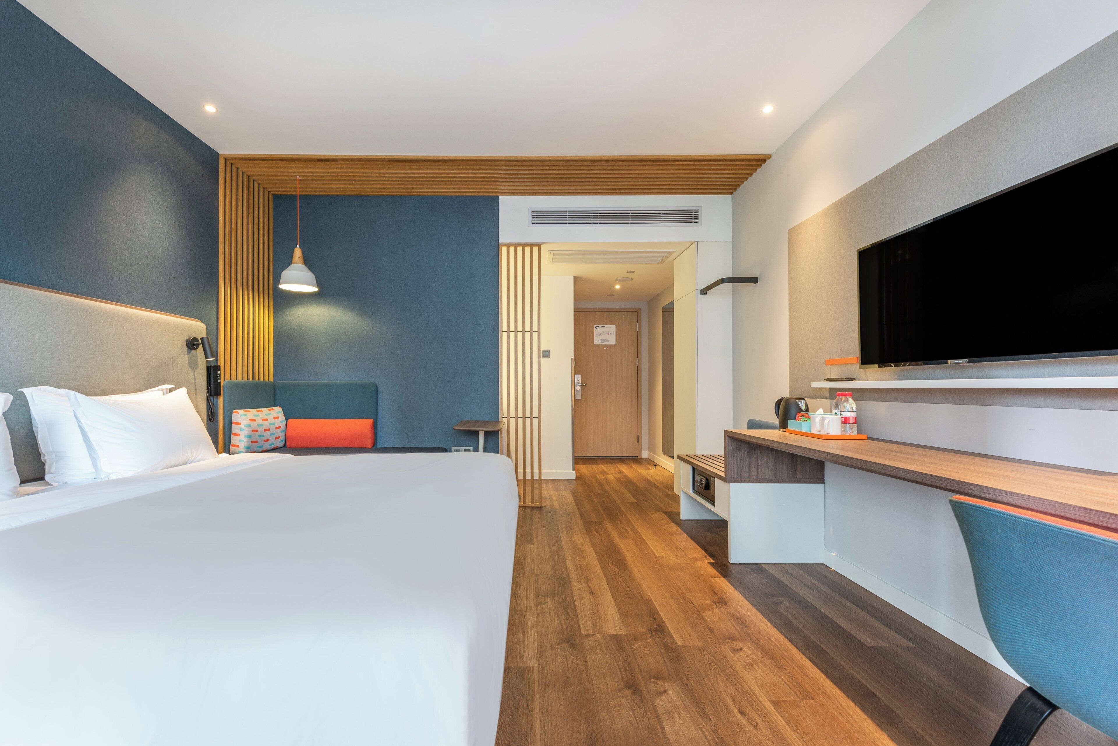 A modern hotel room with a large bed, a desk, a television, and a view of the hallway.
