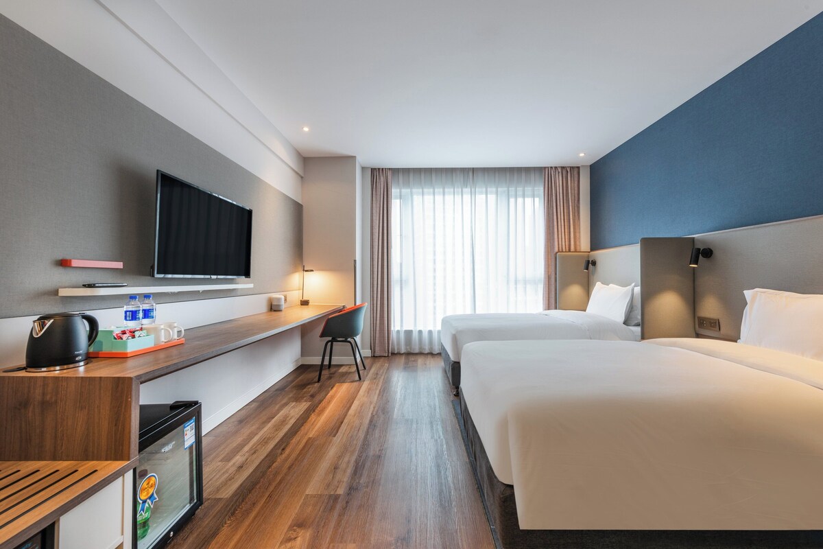 A hotel room with a bed, a desk, a television, and a window with curtains.