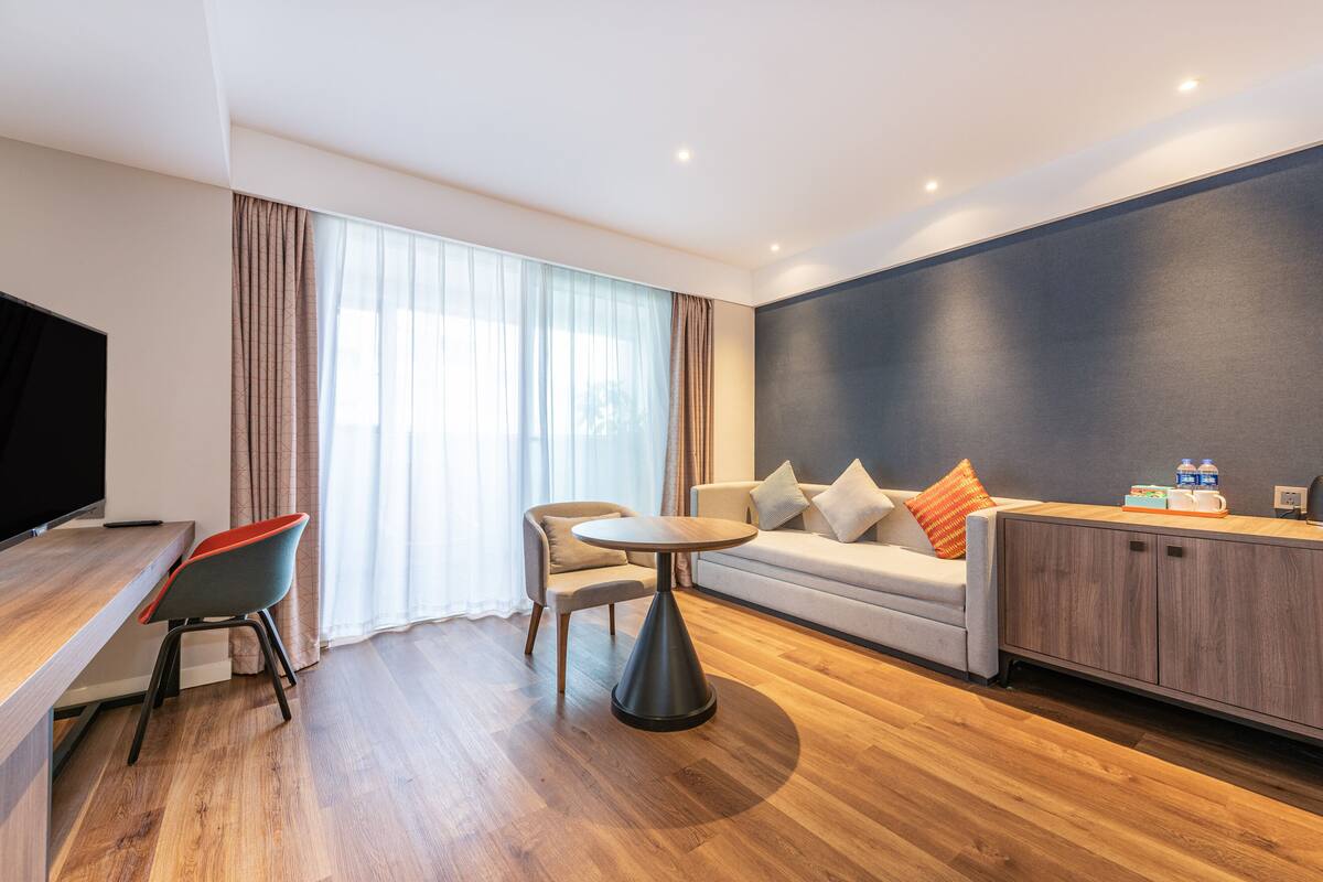 Une chambre d’hôtel moderne avec un plancher en bois, un canapé, une table à manger et un téléviseur.