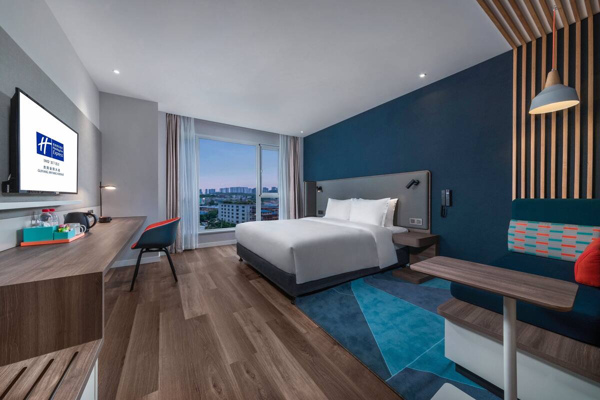Une chambre d’hôtel moderne dotée d’un grand lit, d’un bureau avec un ordinateur, d’une télévision et offrant une vue sur la ville.