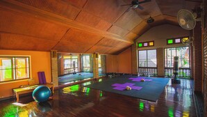 A spacious room with wooden flooring, large windows, and exercise mats. - Joy's House (Chiang Mai)