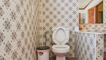 Een badkamer met patroontegels, een toilet, een prullenbak en een rode welkomstmat.