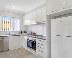 A modern kitchen with white cabinetry, a built-in oven, microwave, and a stainless steel refrigerator. - Scott Street Couples Getaway (ANNA BAY)