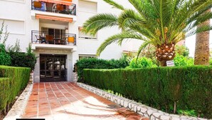 A building with a gated entrance, a balcony with outdoor seating, and a well-maintained garden with a palm tree. - Great apartment with pool in Los Boliches (FUENGIROLA)