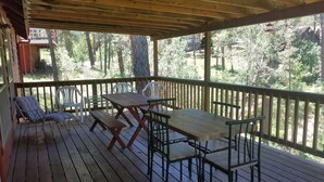 Une terrasse en bois, agrémentée de tables et de chaises pour pique-nique, entourée d’une balustrade en bois, et offrant une vue sur une zone boisée.