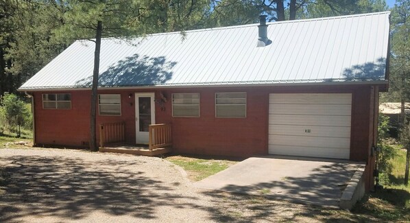 En envåningsbyggnad med en röd fasad, en vit garageport och en liten veranda med en bänk.