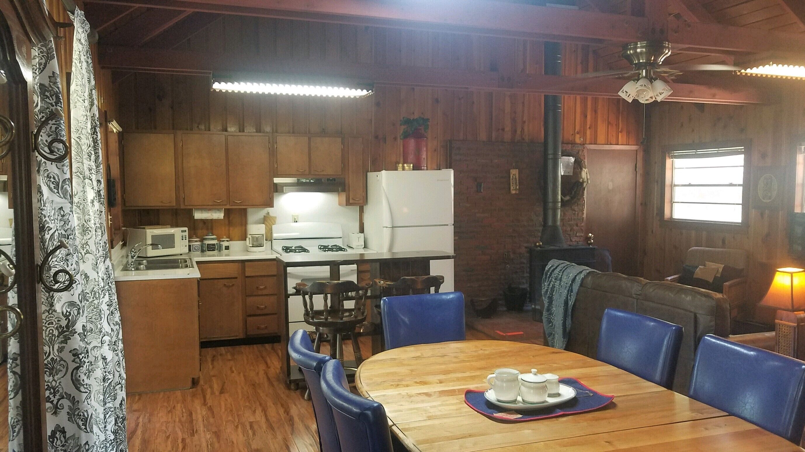 Una cocina acogedora de estilo rústico con armarios de madera, un refrigerador, una estufa y una mesa de comedor con sillas azules.