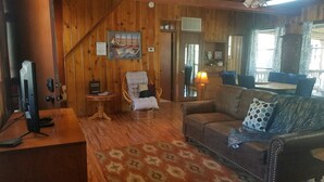 Un salon chaleureux avec des murs en bois, un canapé, un fauteuil, une petite table et un téléviseur.