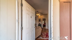 A hallway with a white door, a ceiling fan, and a red patterned rug.