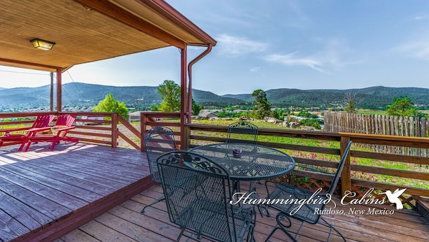 A wooden deck with outdoor seating, a pergola, and a view of a mountainous landscape.
