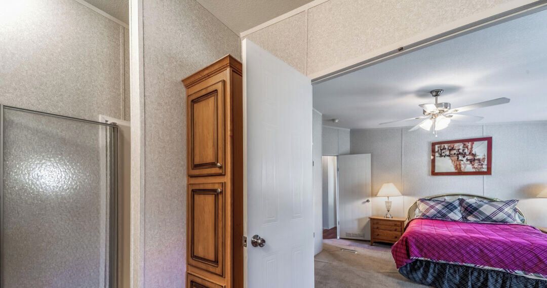 Ein Schlafzimmer mit einem Bett, einem Nachttisch, einem Deckenventilator und einer Tür zu einem weiteren Raum.