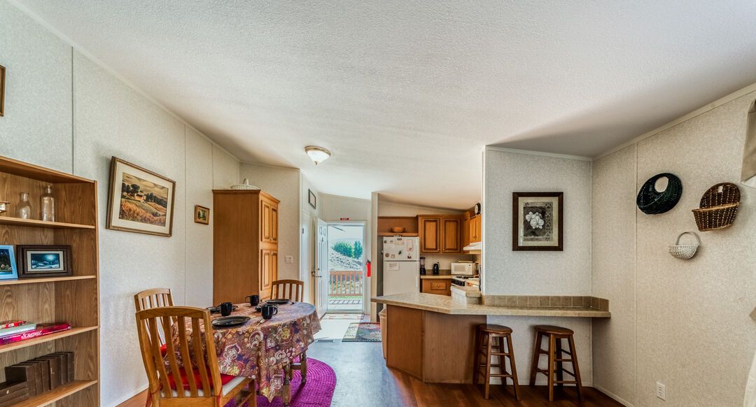 A compact kitchen with wooden cabinets and a central island, a dining area with a table and chairs, and a bookshelf.