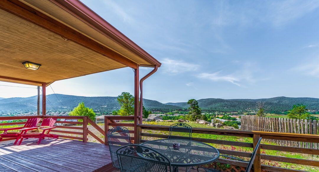 A wooden deck with outdoor seating, a pergola, and a view of a mountainous landscape.