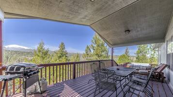 A covered outdoor deck with a grill, metal chairs, and a table.