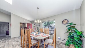 Un comedor con una mesa y sillas de madera, una araña y un amplio ventanal con vista a la calle.