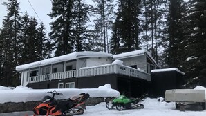 Un edificio di due piani con un balcone, circondato da terreno innevato e alberi alti.