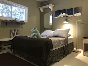 A bedroom with a bed, a nightstand, a lamp, a mirror, and artwork on the wall. - Ski and Sled Vacation Home (Golden)