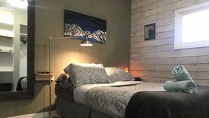 Un letto rifatto con biancheria a motivi decorativi, una lampada da terra, un quadro appeso al muro e una finestra con vista.