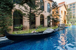 Une gondole dans un espace piscine, avec un bâtiment doté de fenêtres en arc et d’un toit recouvert de tuiles.