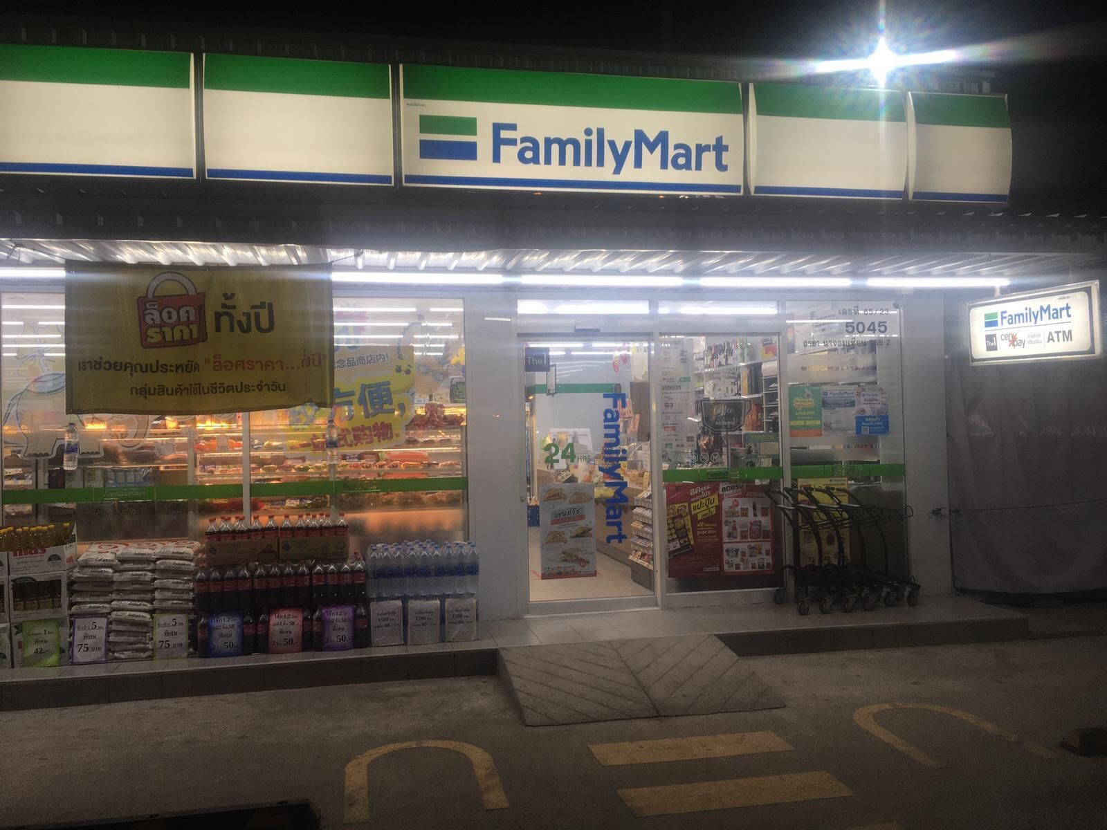 A FamilyMart store at night with a visible entrance, shelves stocked with products, and an ATM on the right.