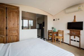 Une chambre d’hôtel avec un grand lit, une armoire en bois, un petit coin repas avec une table et des chaises, un téléviseur posé sur un meuble en bois et un climatiseur fixé au mur.