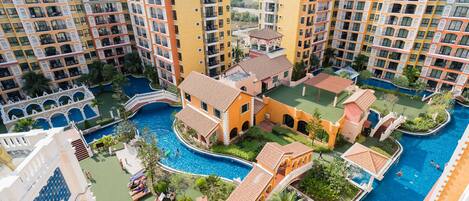 A multi-story hotel with a central courtyard featuring a swimming pool, surrounded by lush greenery and palm trees.