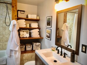 A bathroom with a sink, mirror, and shelves with towels and toiletries. - Cozy Log Cabin on 2 acres, backs to Pike National Forest, just 15mi to Breck (Alma)