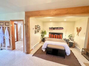 A bedroom with a large bed, a wooden headboard, a bedside table with a lamp, and a wall-mounted shelf with decorative items. - Cozy Log Cabin on 2 acres, backs to Pike National Forest, just 15mi to Breck (Alma)