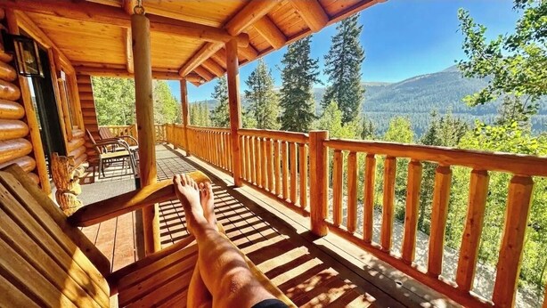 Una terraza de madera con barandilla, con vista a una zona montañosa boscosa.
