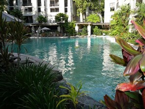 A pool surrounded by lush greenery and a multi-story building with balconies. - Luxury Apartment at Sea Temple Palm Cove 2 Bed 2 Bath (Palm Cove)