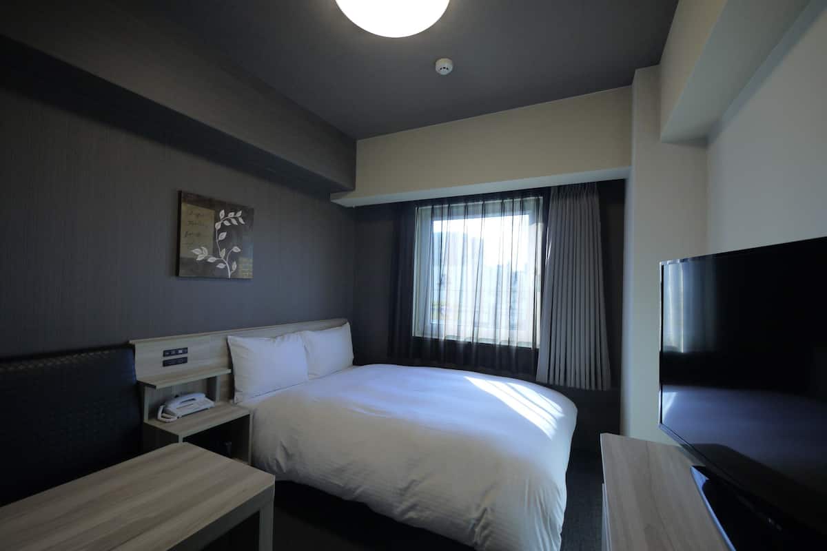 Ein Hotelzimmer mit Bett, Nachttisch, Fernseher und einem Fenster mit Vorhängen.